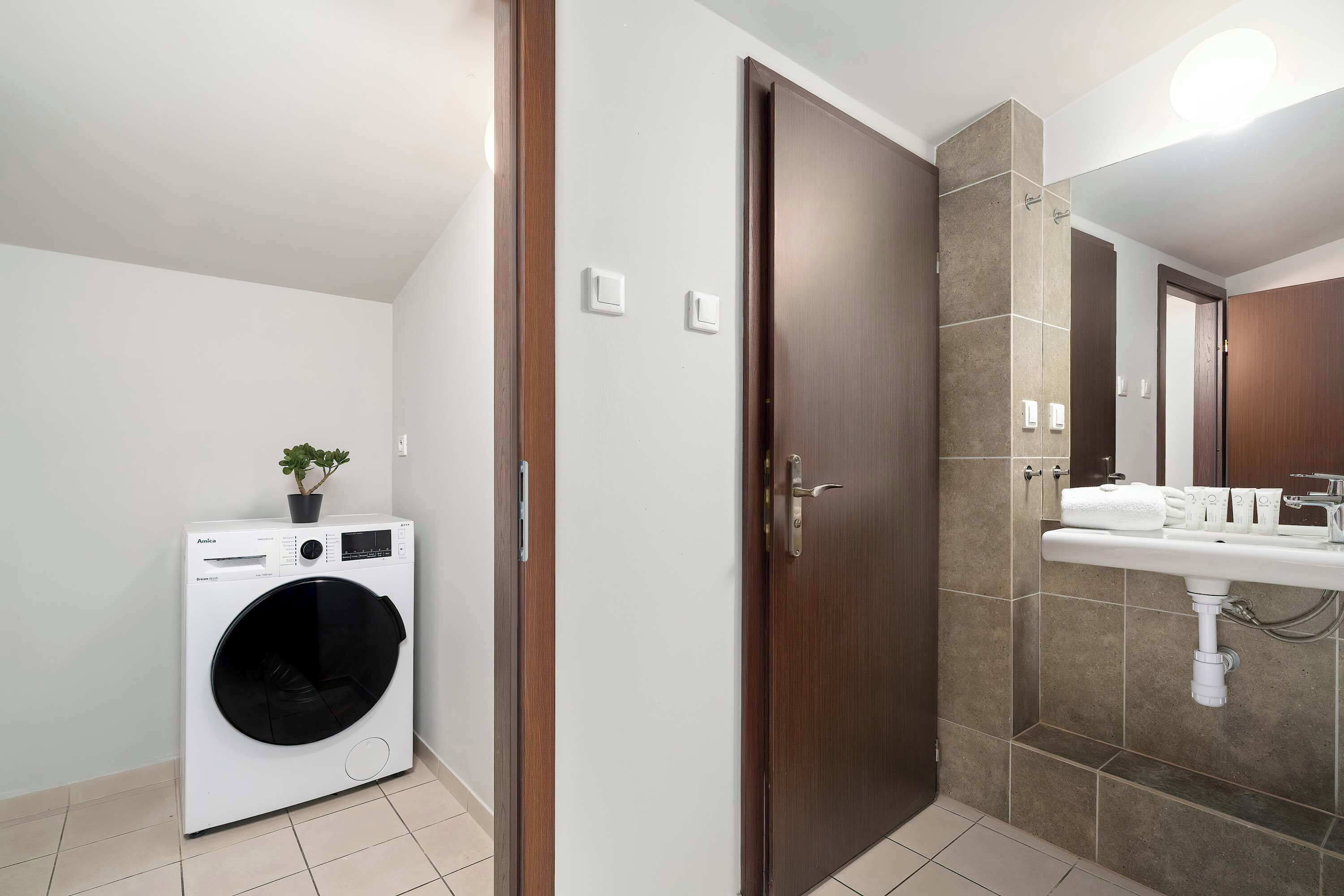 Une petite salle de bain équipée d’un lave-linge encastré, d’une porte en bois et d’un plan-vasque carrelé.