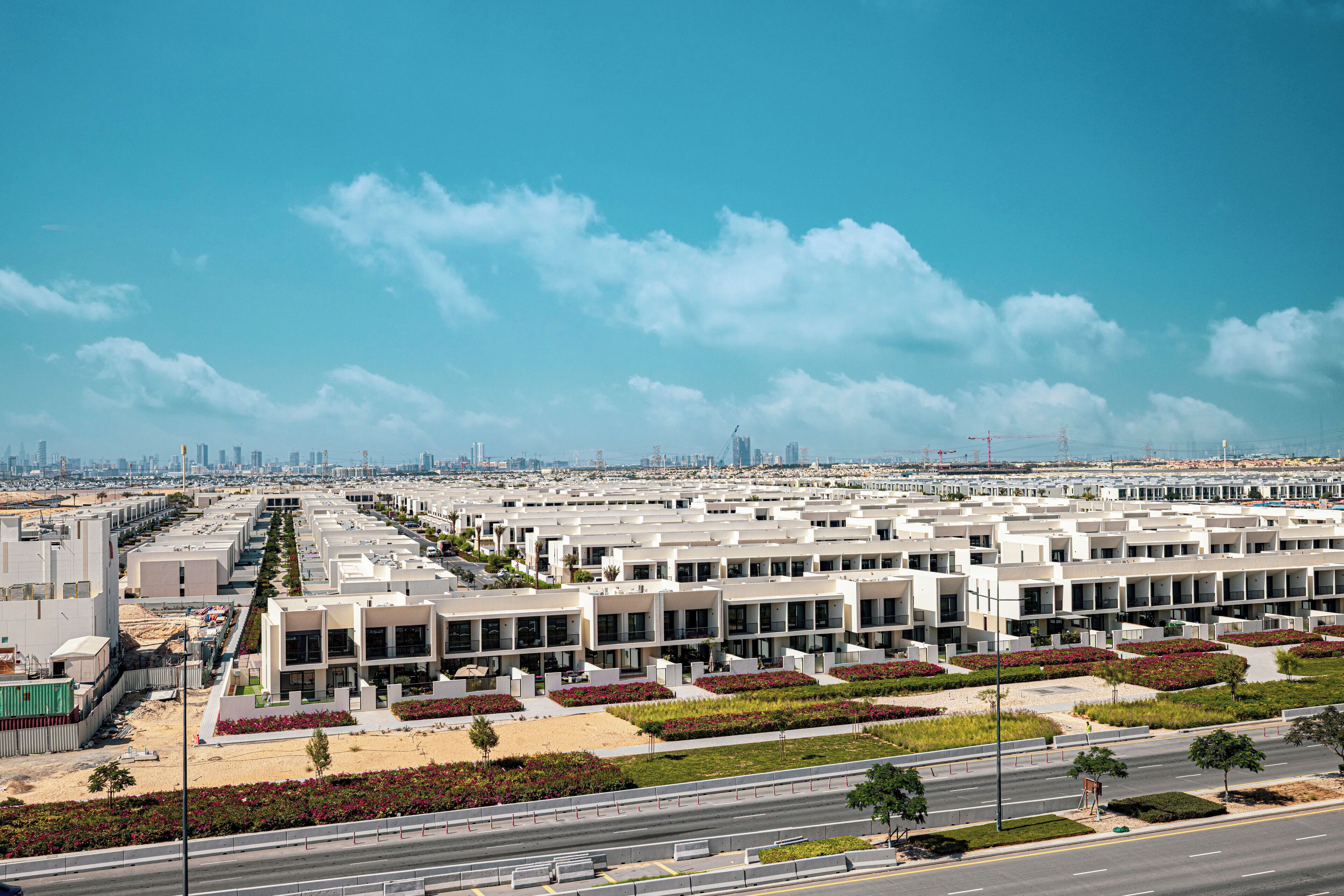 A modern urban development with a series of white buildings, green landscaped areas, and a clear blue sky.