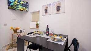 A dining area with a table set for two, a television mounted on the wall, and artwork above the table. - Kyma Luxury Apartment - Sea & Taormina, Giardini Naxos, Sicily (Giardini Naxos)
