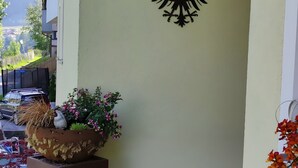 Gevel van een gebouw met een grote plantenbak vol diverse planten en bloemen, een metalen wanddecoratie en een uitzicht op een woonwijk op de achtergrond.