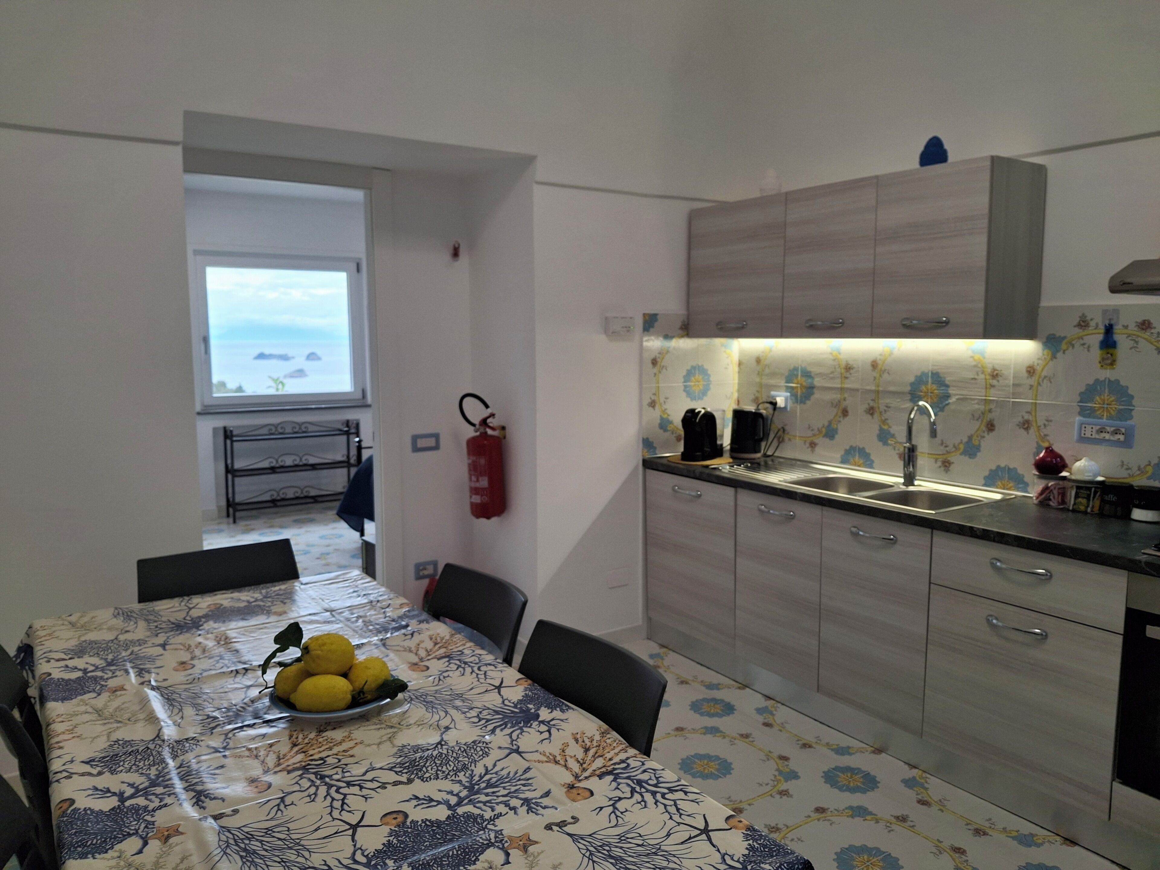 Uma cozinha com uma mesa de jantar posta para quatro pessoas, uma cafeteira e um extintor de incêndio na parede.
