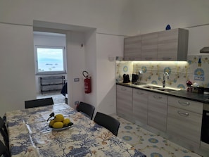 A kitchen with a dining table set for four, a coffee maker, and a fire extinguisher on the wall. - Rosa House - House in the picturesque landscape of Nerano (Campania)