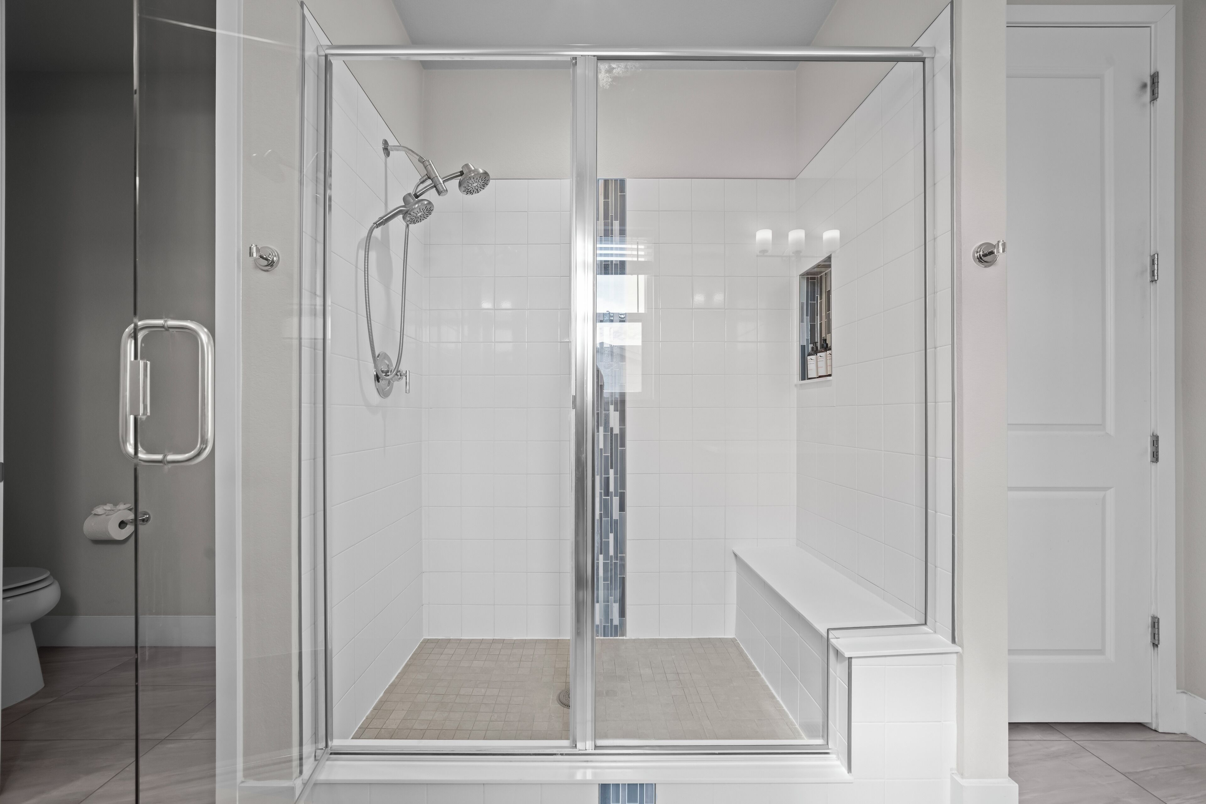 A modern bathroom with a glass-enclosed shower, white tiles, and a visible toilet.