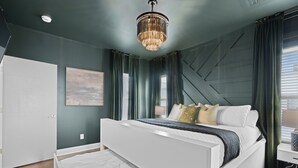 Ein modernes Schlafzimmer mit einem großen Bett, einer Chandelieber und Blick ins Freie.
