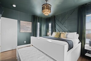 Ein modernes Schlafzimmer mit einem großen Bett, einer Chandelieber und Blick ins Freie.