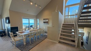 Un vaste espace de vie comprenant une table à manger, des chaises, une cheminée, une grande fenêtre et un escalier.