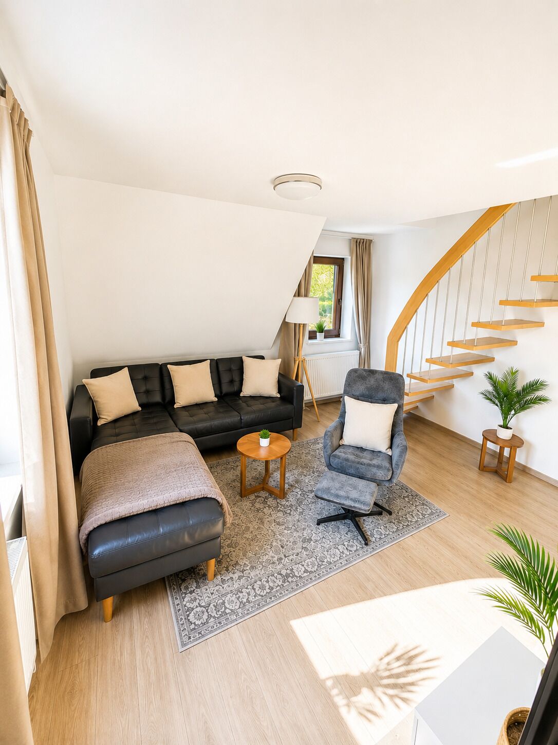 A modern living room with a black sofa, a grey armchair, a small round table, and a staircase with wooden steps.