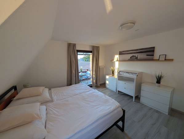 A bedroom with a bed, a desk, a dresser, and a window with curtains.