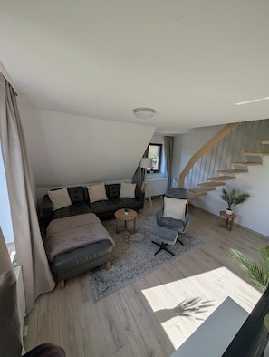 A modern loft bedroom with a sloped ceiling, a built-in staircase, a sofa bed, a chair, and a small table.