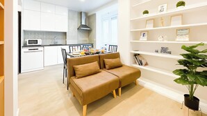Eine moderne Küche mit weißen Schränken, eine Essecke mit einem braunen Sofa und ein Bücherregal mit verschiedenen Gegenständen.