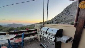 Eine Terrasse im Freien mit einem Edelstahlgrill, einem Tisch mit Stühlen und Blick auf die Berge.