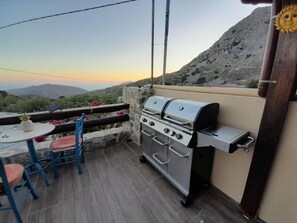 Eine Terrasse im Freien mit einem Edelstahlgrill, einem Tisch mit Stühlen und Blick auf die Berge.