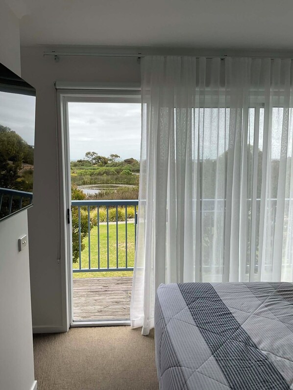 Une chambre avec un lit, un balcon donnant sur un espace verdoyant et des arbres, et des rideaux légers.