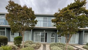 A two-story building with a central entrance, surrounded by a gravel pathway, small bushes, and two trees. - Bay & wetland views in beautiful Williamstown, Relax, unwind and enjoy (Williamstown)