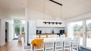 Uma cozinha moderna com armários brancos, uma área de refeições com cadeiras brancas e uma janela grande que oferece vista para o exterior.