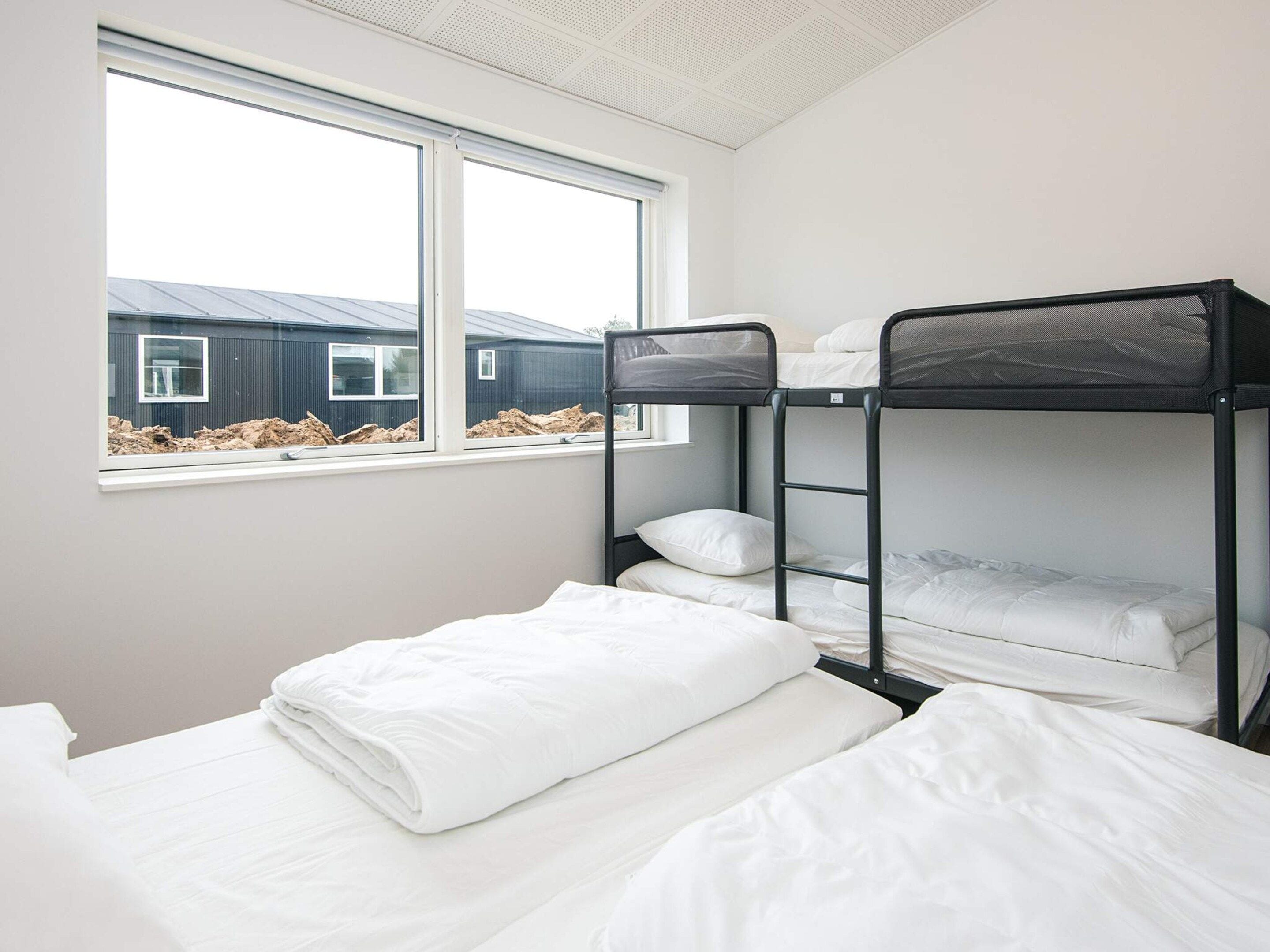 Une chambre avec un lit superposé, une fenêtre, du linge de lit blanc et une vue sur un bâtiment à l’extérieur.