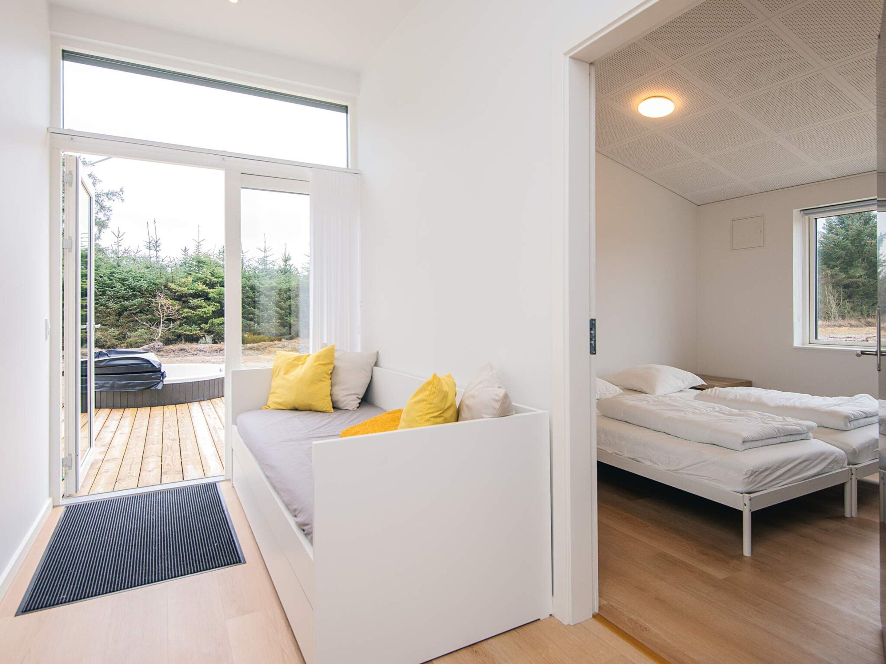 Een modern interieur met een slaapbank, een tweepersoonsbed en uitzicht op een bos door een groot raam.