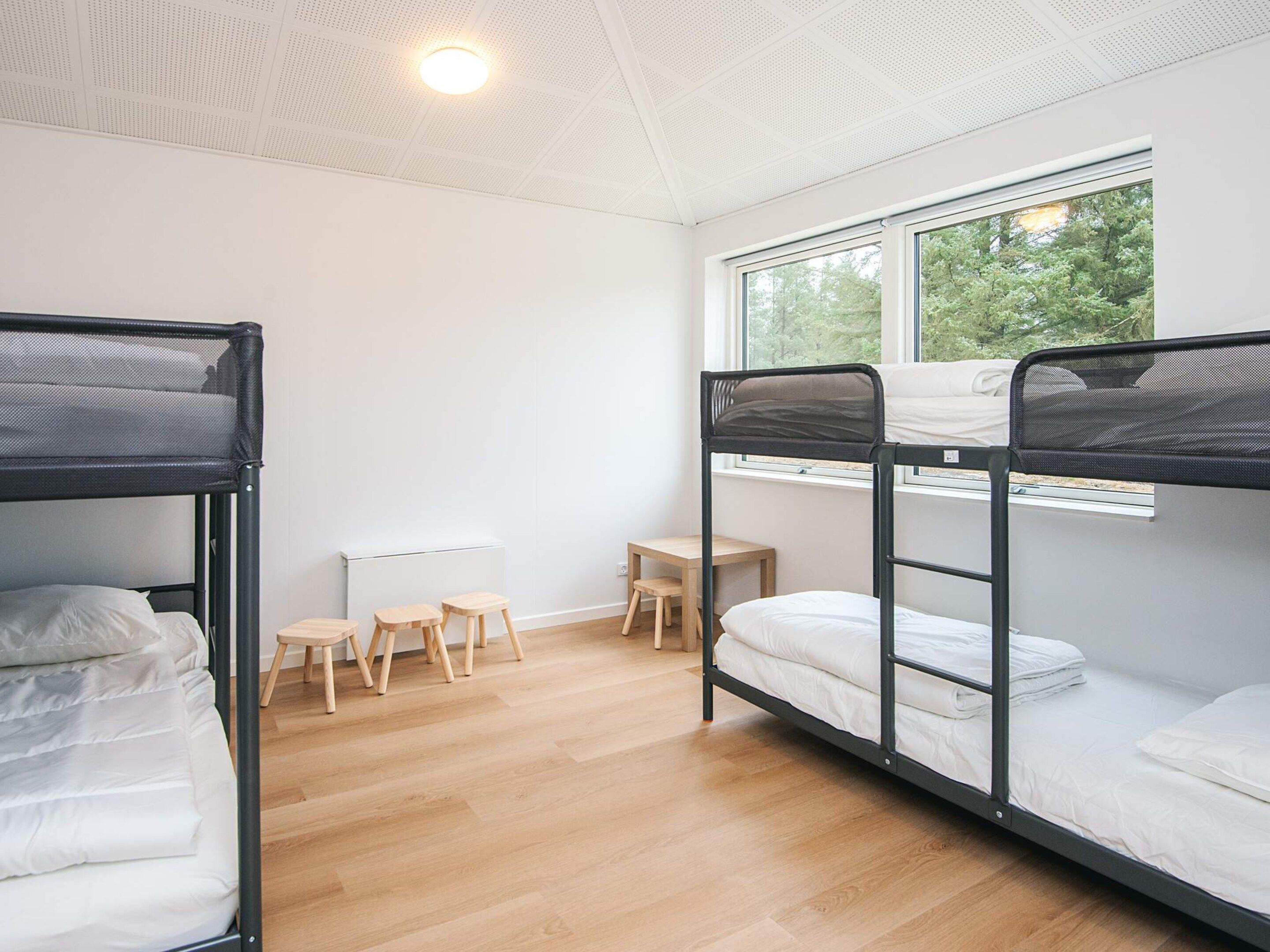 Une chambre de dortoir avec des lits superposés, un bureau et une fenêtre donnant sur les arbres.