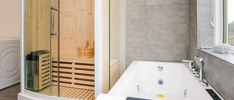 A modern bathroom with a glass-enclosed sauna, a large bathtub, and a window with a view.