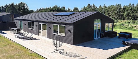 A modern house with a deck, outdoor seating, and a large window.