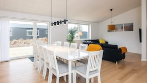 Sala de estar moderna com área de jantar, janelas amplas e vista para uma construção em andamento ao ar livre.