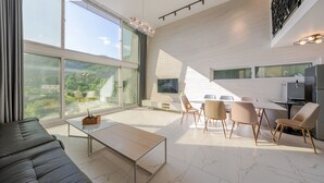 A modern living room with a large window, a flat-screen TV, a dining area with chairs, and a kitchen area with a refrigerator. - Gapyeong Abek J Pool Villa (Gapyeong)