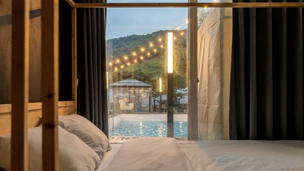 A bedroom with a large window overlooking a pool and outdoor area. - Gapyeong Abek J Pool Villa (Gapyeong)