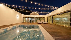 An outdoor swimming pool area with a wooden deck, lounge chairs, and string lights. - Gapyeong Abek J Pool Villa (Gapyeong)