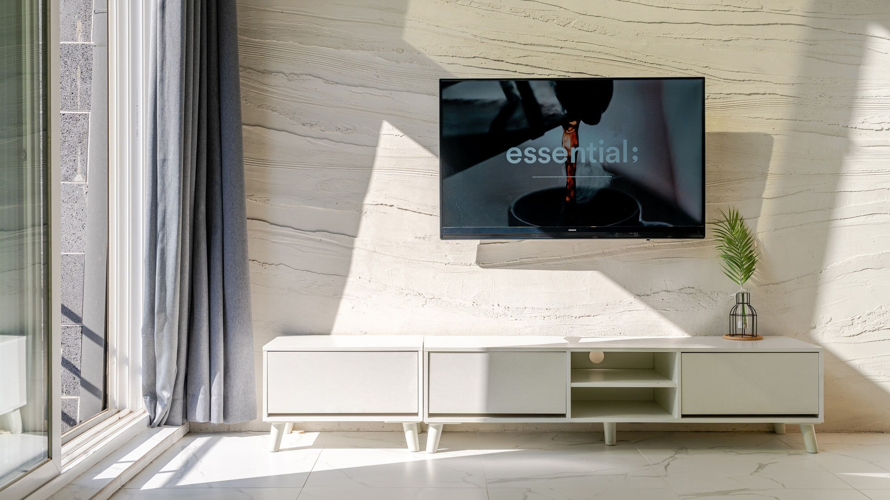 Een moderne woonkamer met een grote flatscreen televisie aan een gestructureerde muur, een witte console tafel en een potplant.