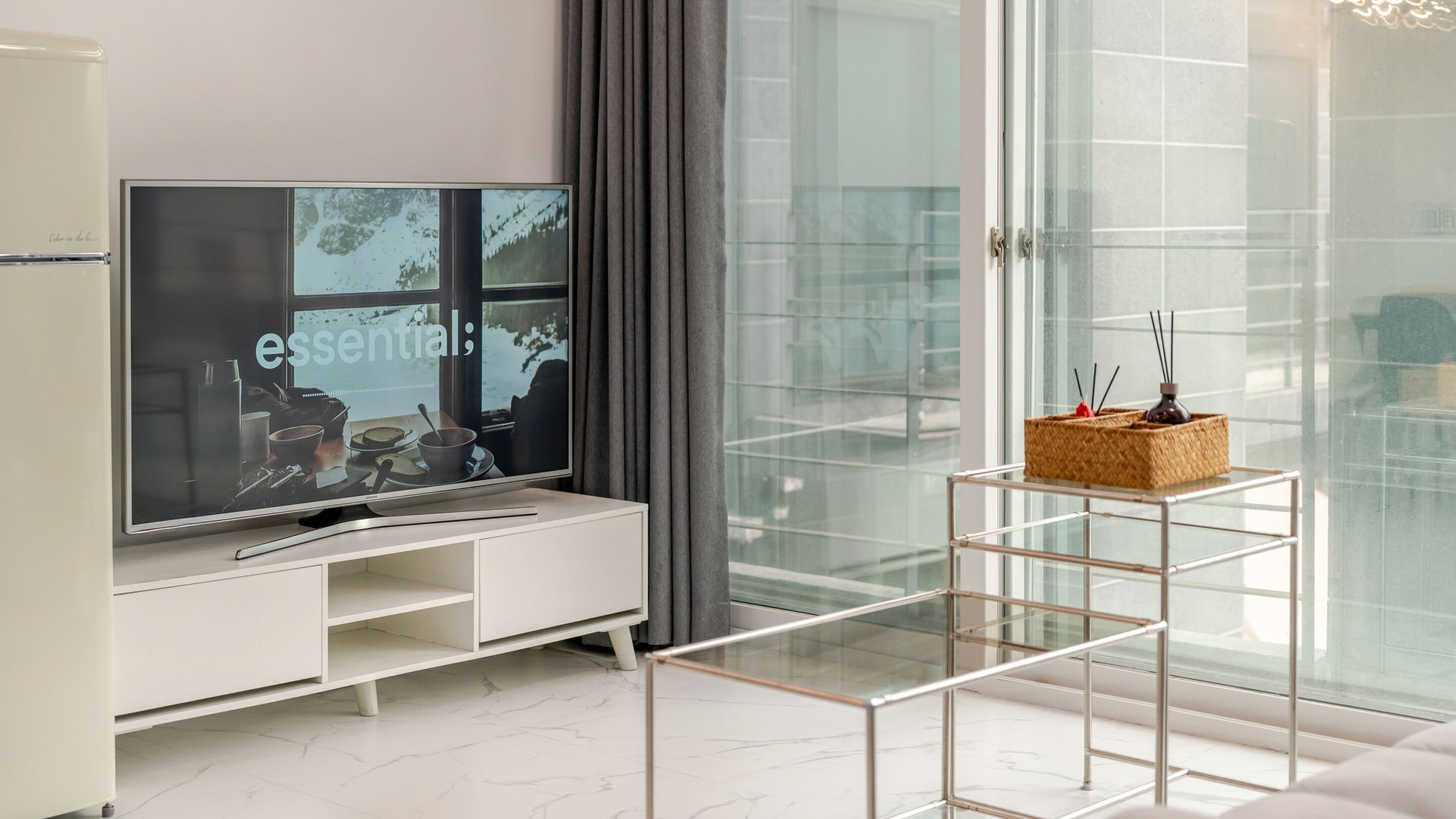A modern living room with a flat-screen TV, a glass coffee table, and a minimalist design.