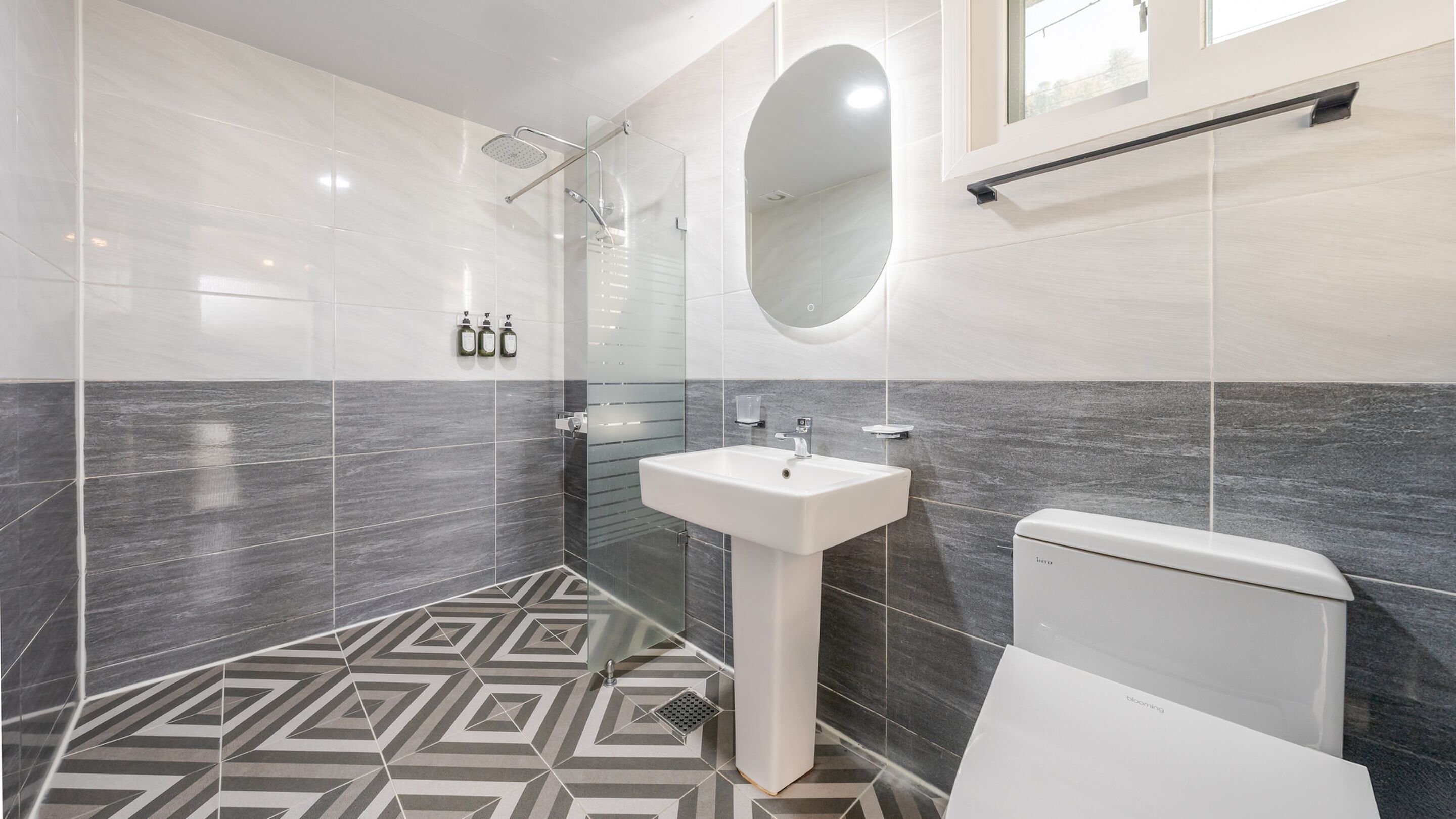 A modern bathroom with a geometric patterned floor, a white sink, a toilet, and a glass-enclosed shower area.