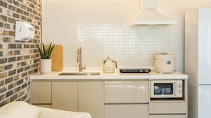 A compact kitchen with a brick wall, a sink, a kettle, a rice cooker, and a built-in oven. - Taean Sagye Pension (Taean)