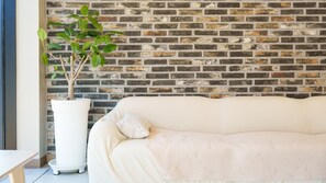 A room with a brick wall, a white sofa, and a potted plant. - Taean Sagye Pension (Taean)