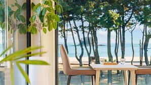 Un espace repas avec une table et des chaises, donnant sur une plage bordée d’arbres et sur la mer.