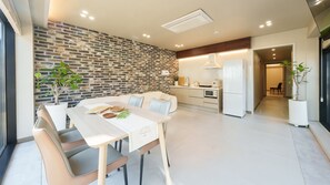 A modern kitchen with a brick wall, a dining area with a white table and chairs, and a visible refrigerator. - Taean Sagye Pension (Taean)