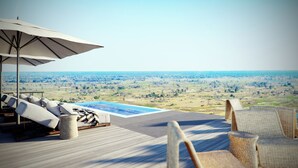 Une terrasse dotée de chaises longues, d’une piscine et offrant une vue sur un vaste paysage.
