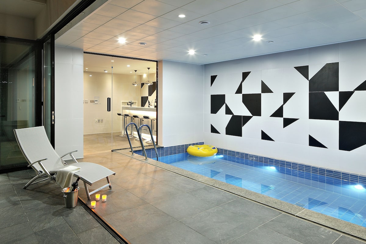 A modern indoor pool area with a lounge chair, a yellow float, and geometric wall designs.