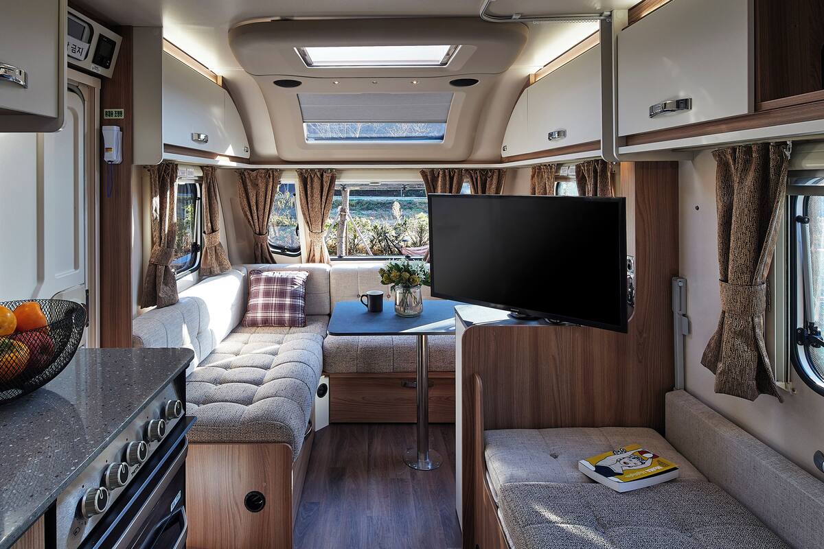 A compact RV interior with a kitchenette, seating area, and a TV.