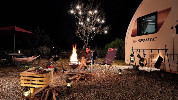 Un campeggio con un focolare, sedie da campeggio e un camper con la scritta "SPRITE".