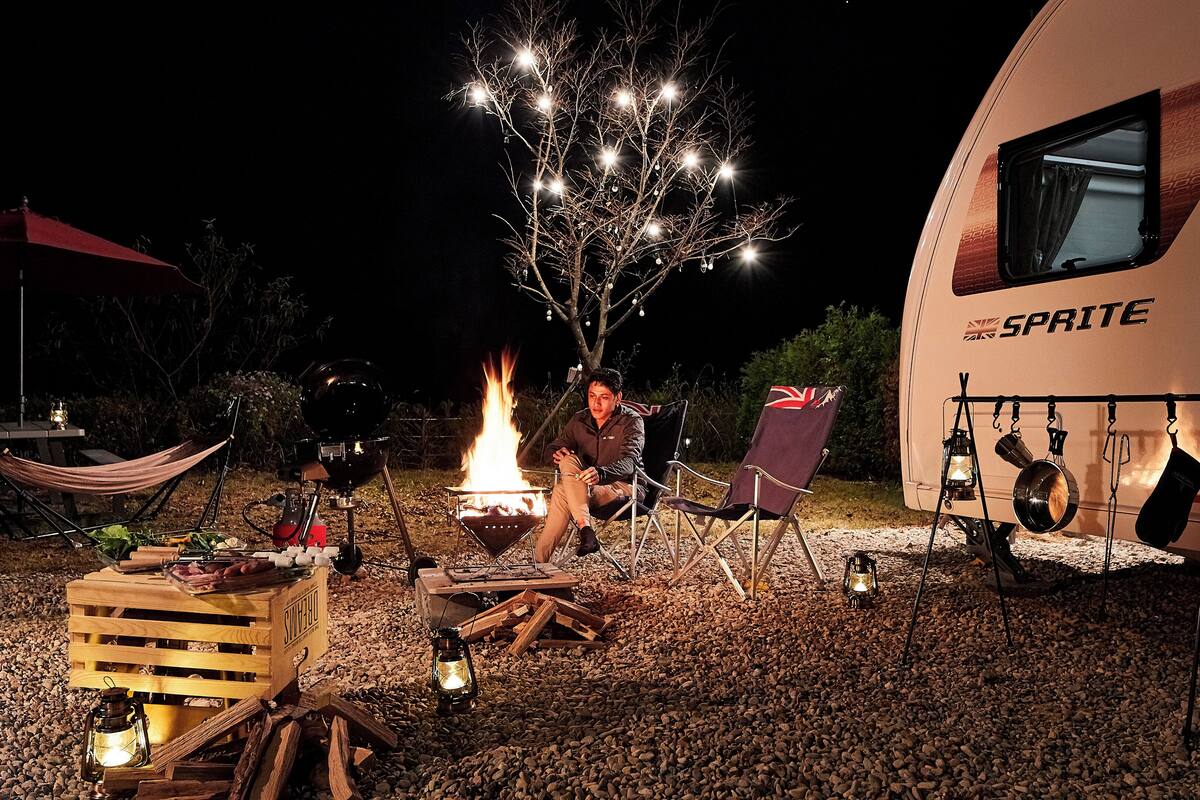 A campsite with a fire pit, camping chairs, and a trailer labeled "SPRITE".