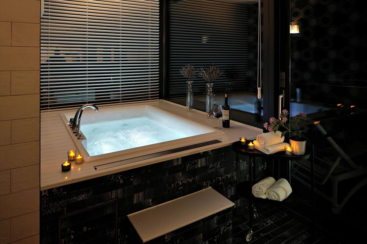 A modern bathroom with a large bathtub, a vanity with a mirror, and a window with blinds.