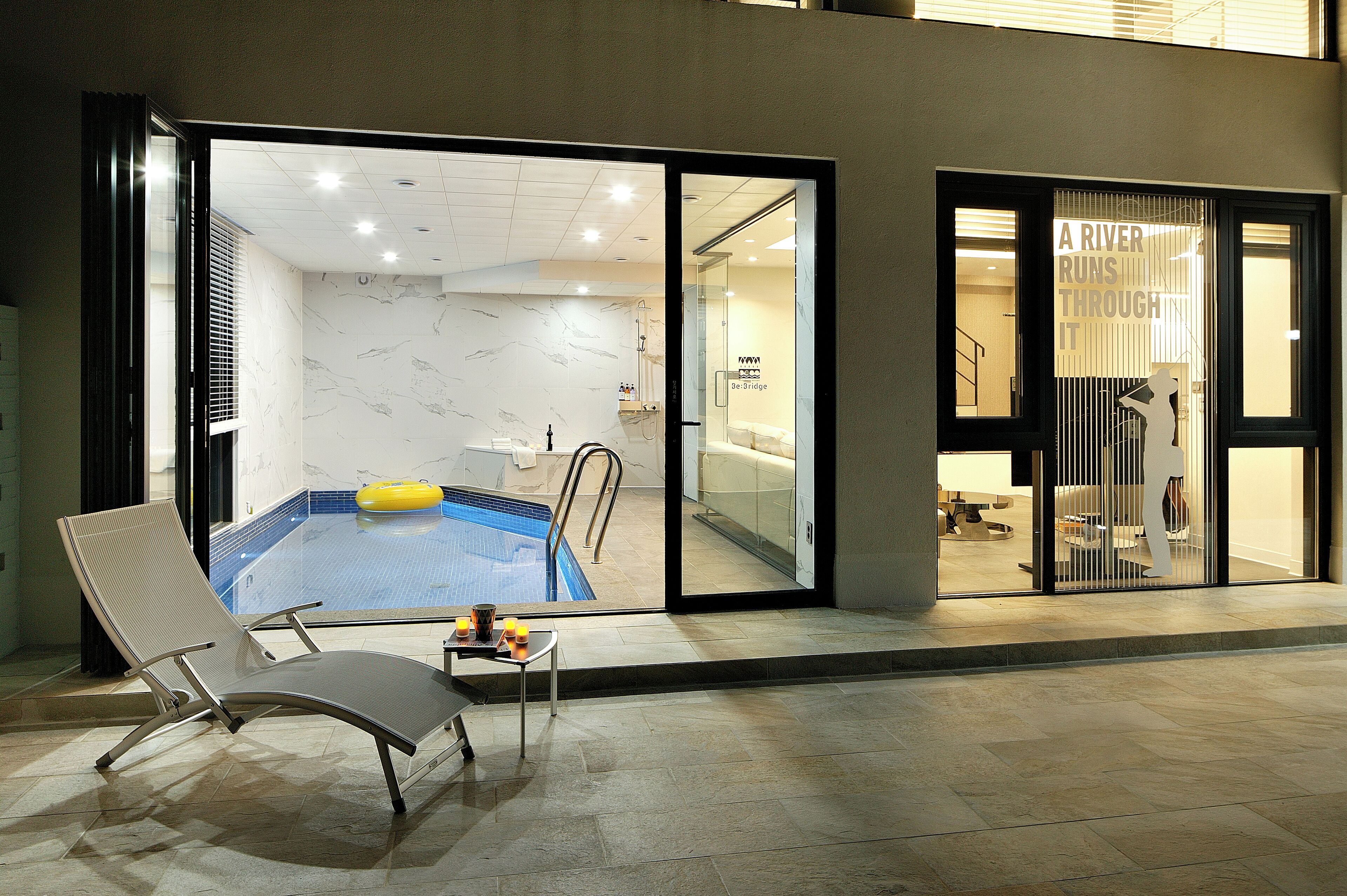Una habitación de hotel moderna con piscina privada, una silla de descanso y una puerta de vidrio que da a la zona de la piscina.