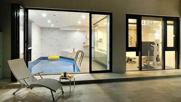 Una habitación de hotel moderna con piscina privada, una silla de descanso y una puerta de vidrio que da a la zona de la piscina.