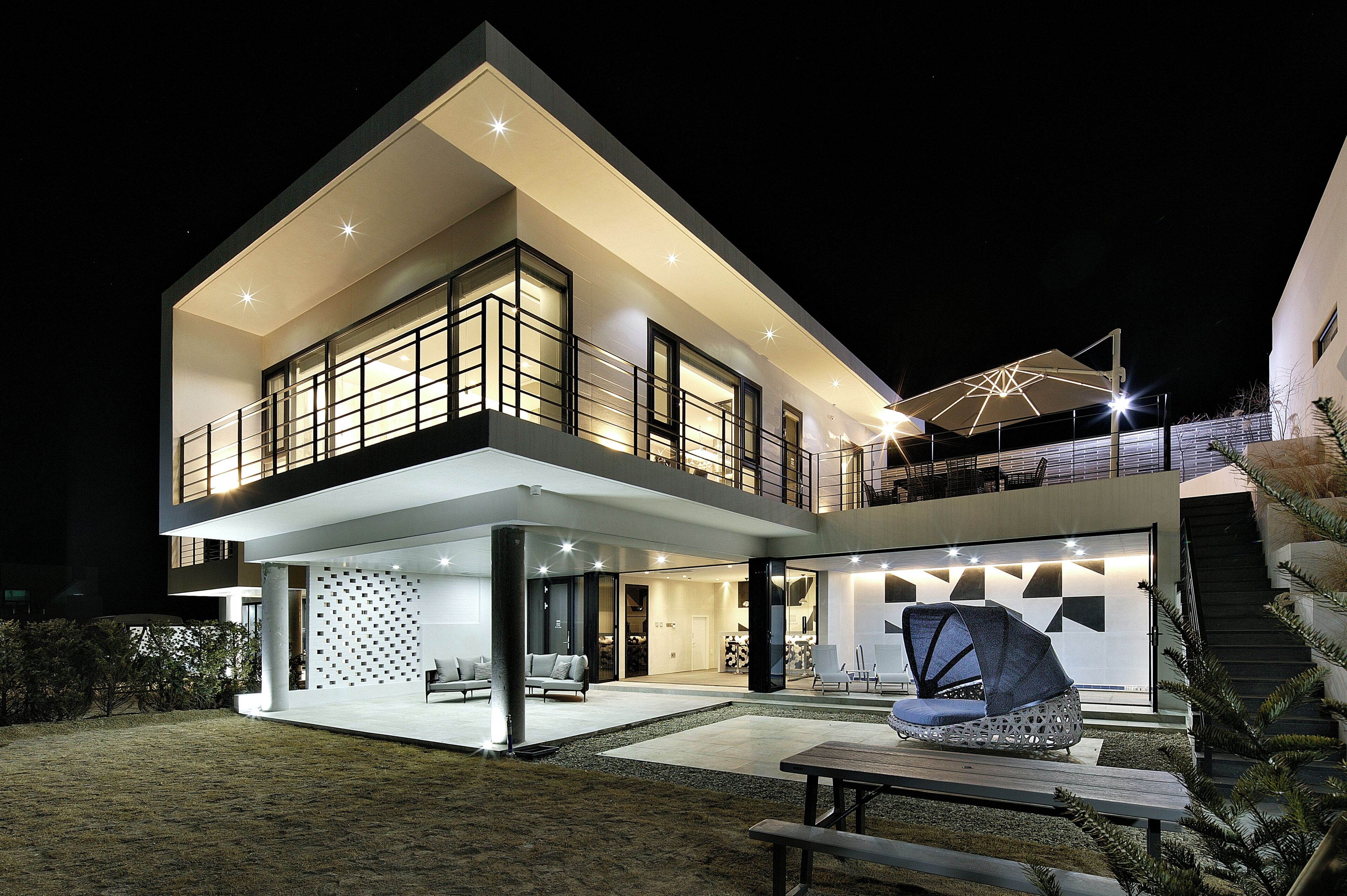 A modern two-story house with a balcony, a covered outdoor seating area, and a staircase leading to the upper level.