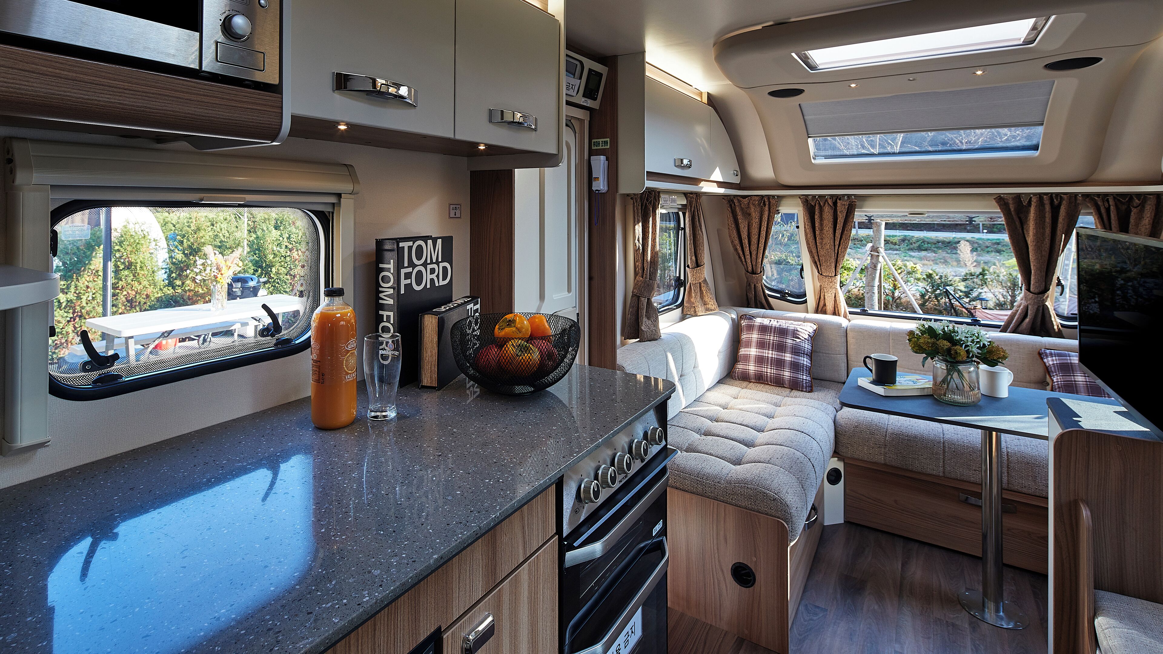 A compact RV interior with a kitchenette, a dining area, and a seating space with a view.