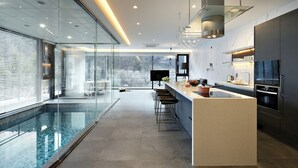 Una cucina moderna con una grande isola, una zona pranzo con sgabelli da bar e un'area piscina vetrata.