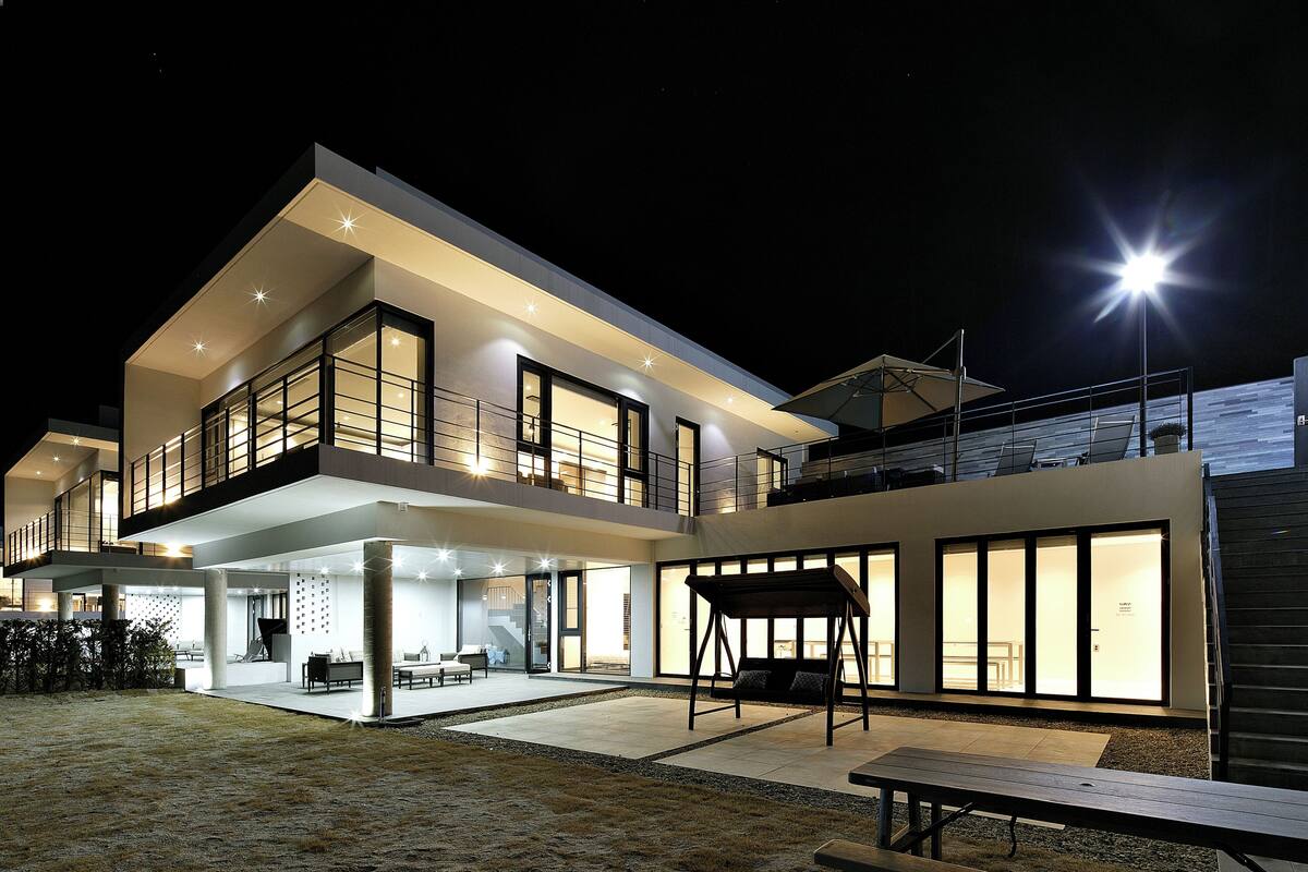 A modern two-story house with a spacious patio, large windows, and a covered seating area.