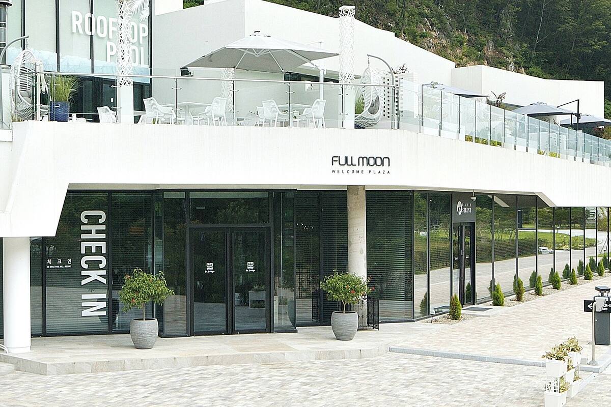 A modern building with a glass facade, outdoor seating, and potted plants.
