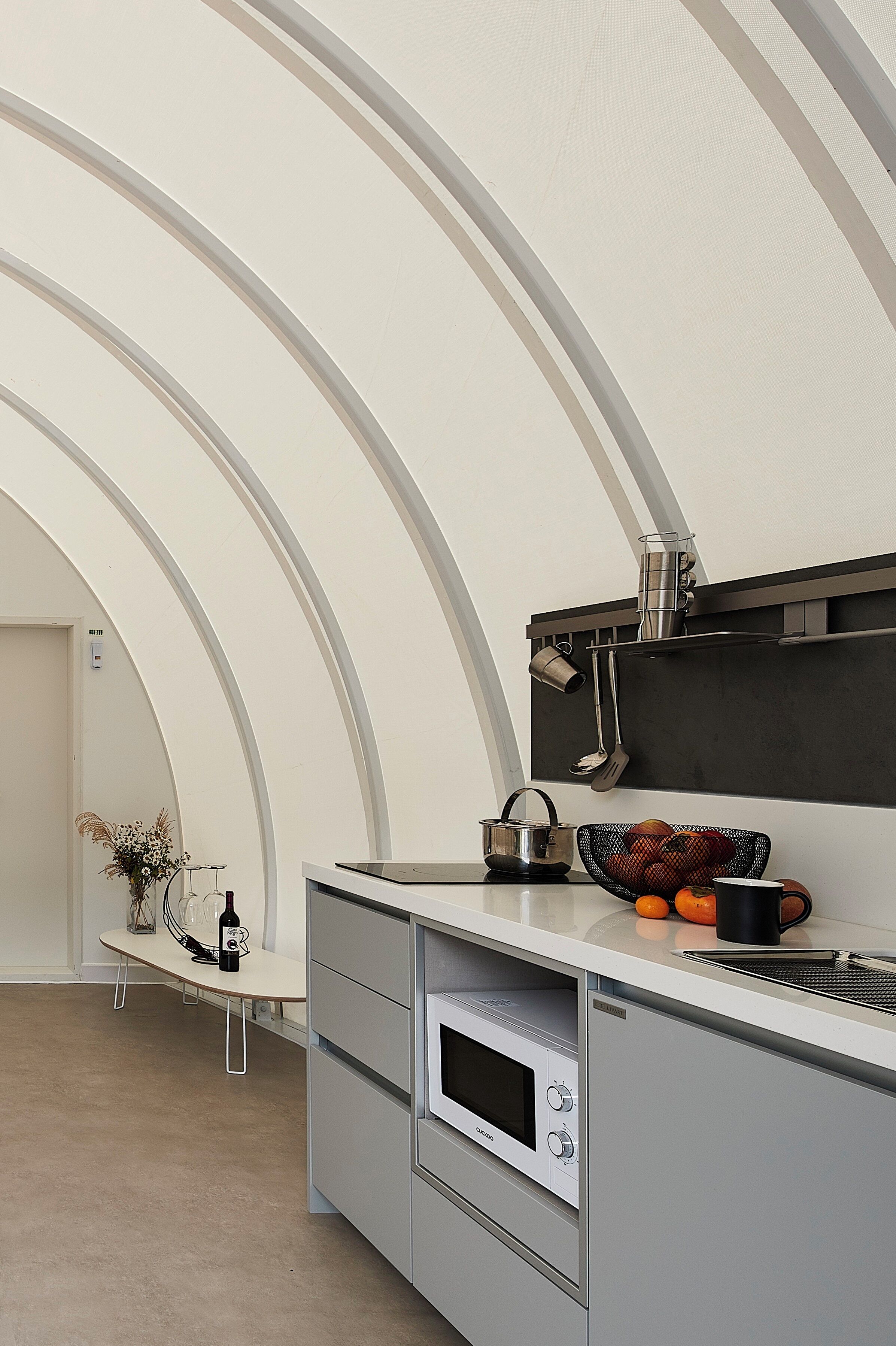 Una cocina moderna con techo curvo, horno empotrado y electrodomésticos de acero inoxidable.