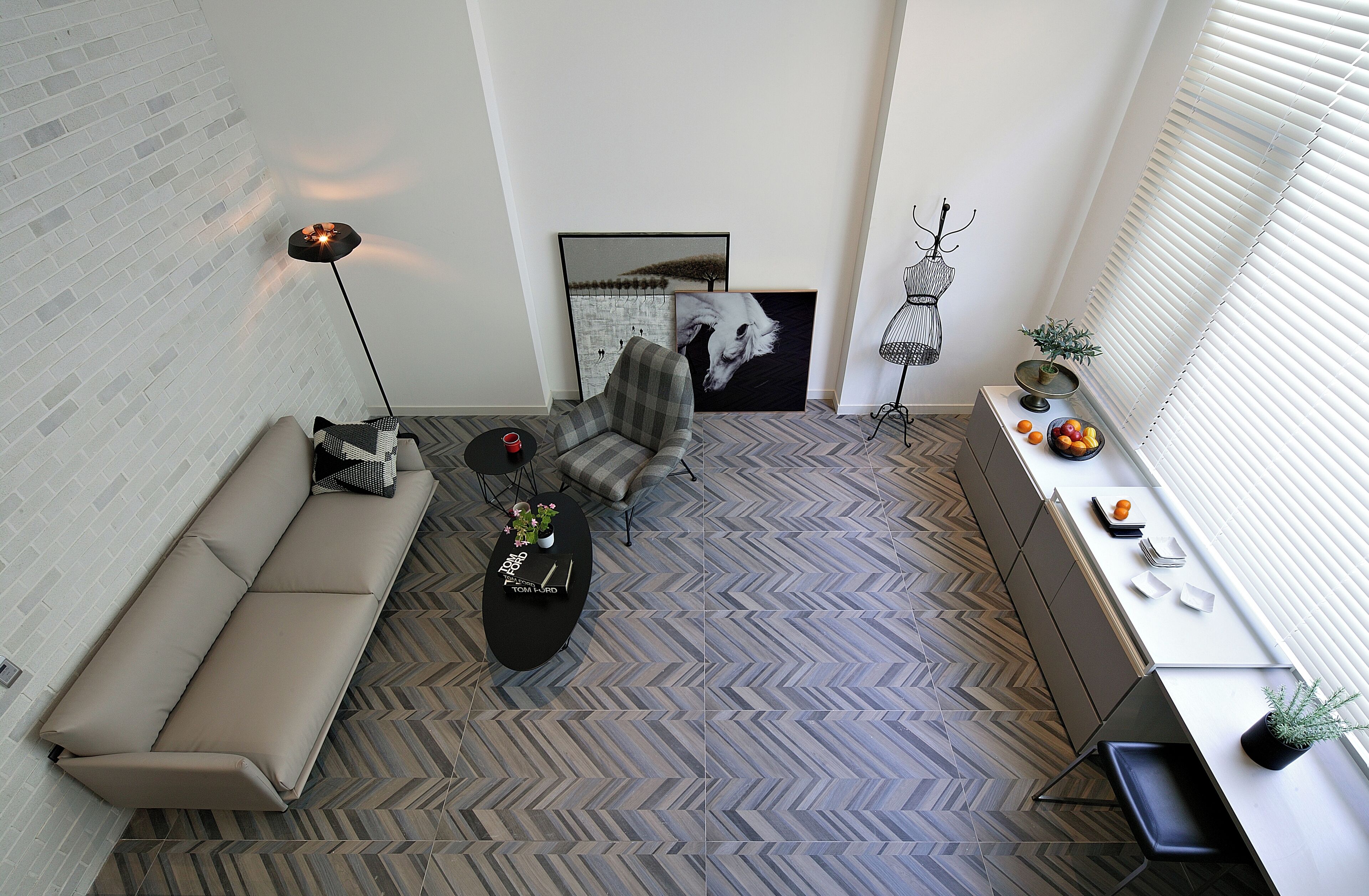 Una sala de estar moderna con un sofá, un sillón y una mesa de centro, un suelo con estampado de espiga y una obra de arte en la pared.